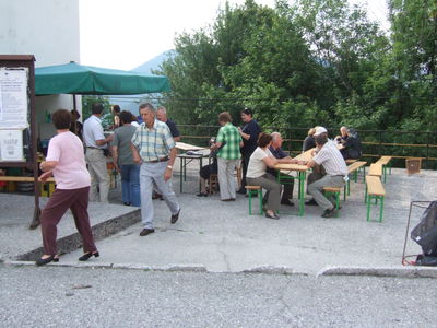 Prostor ob Krajevni skupnosti z mizami in klopmi, pod dežnikom sta kuhinja in prodaja pijač (D868)